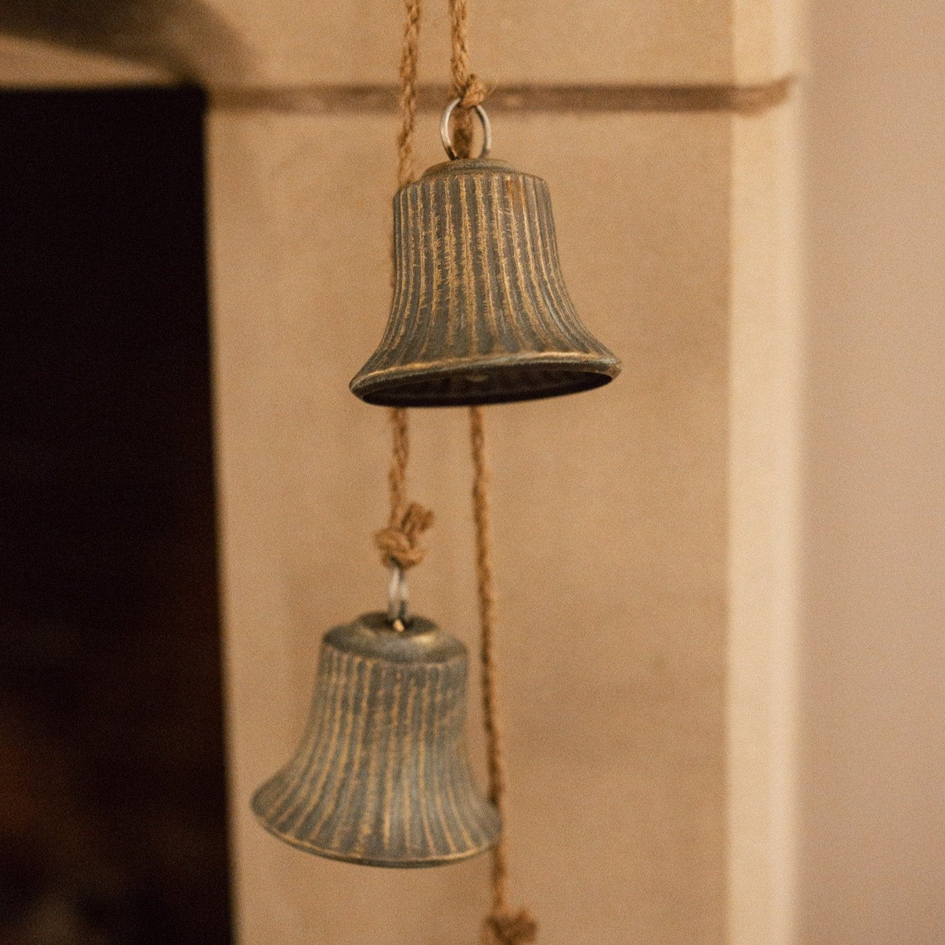 Close up rustic aged brass 3 bell garland hanging from a mantlepiece.