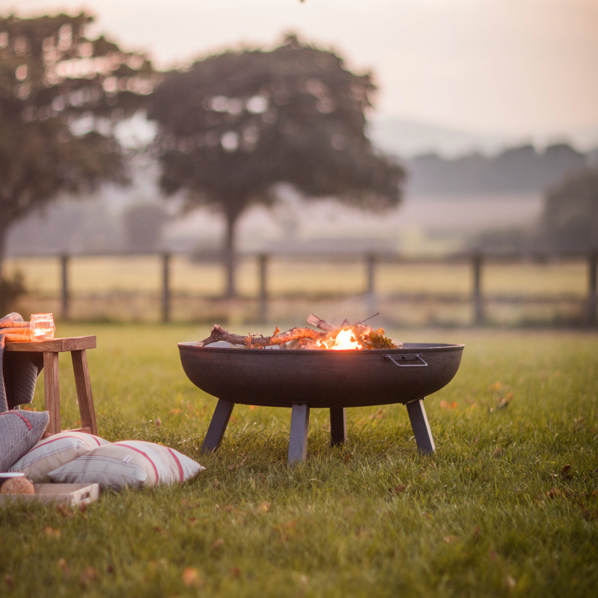 rustic metal fire pit in sunset field with cushions.