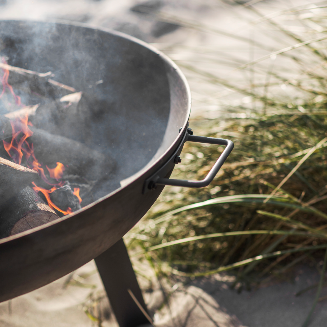 Detailed shot of metal fire pit with logs on the beach.