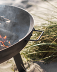 Detailed shot of metal fire pit with logs on the beach.