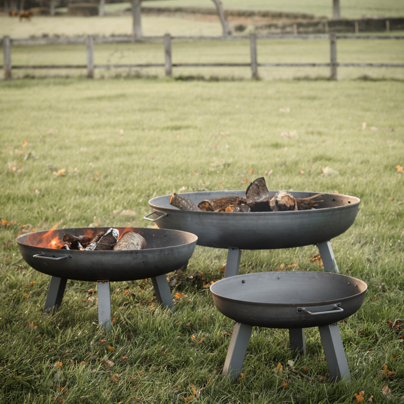 three varying sizes of metal fire pits on a garden field. 