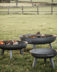 three varying sizes of metal fire pits on a garden field. 