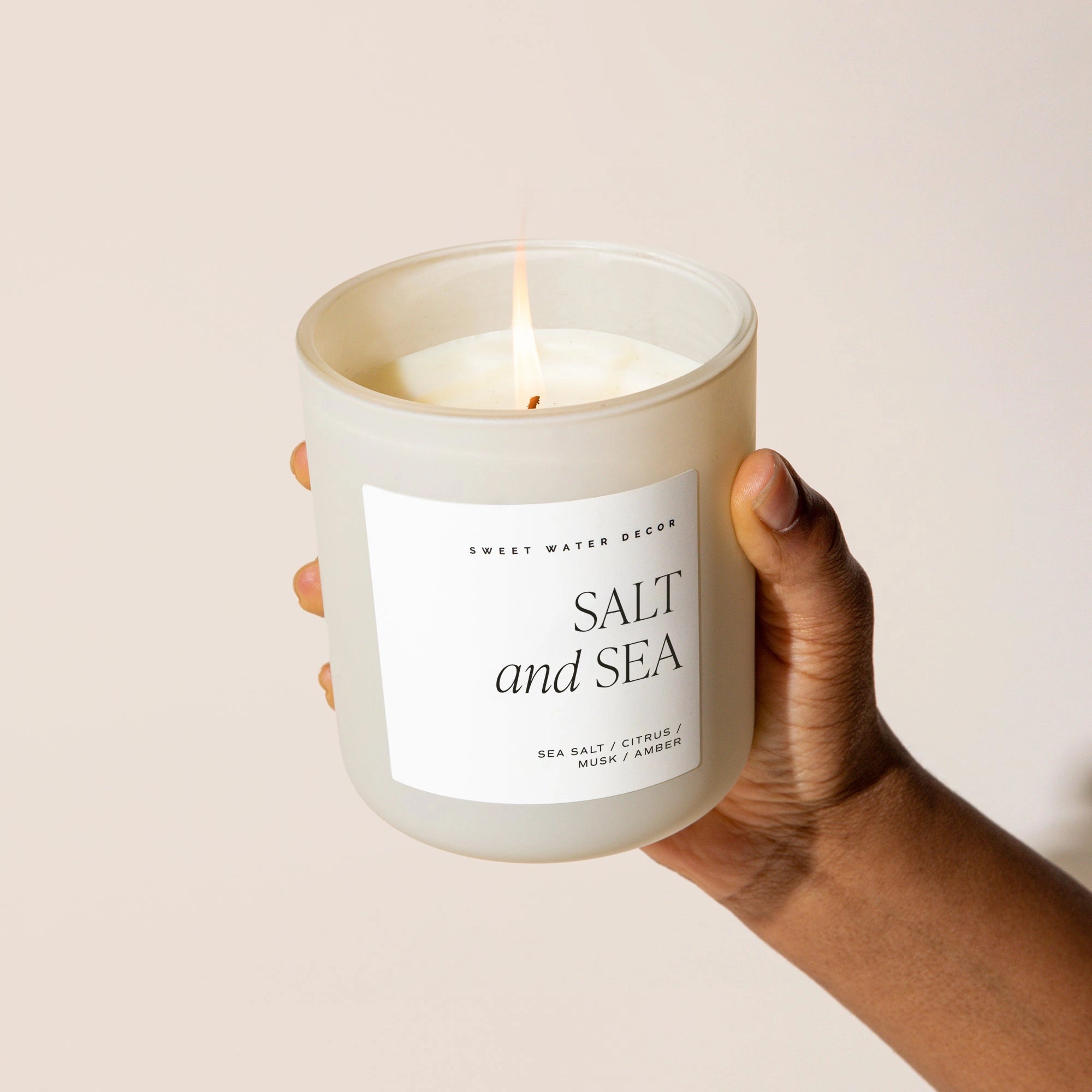 Salt and sea soy candle in white matt jar, held up and lit.