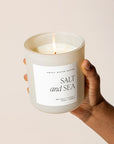 Salt and sea soy candle in white matt jar, held up and lit.