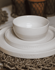 a dinner place setting with cream crockery on a wicker placemat.