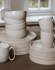 cream crockery set with plates, mugs and bowls stacked on wooden table.
