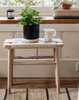 Lulworth Rustic Wooden Side Table against a panelled wall, there is a plant and a mug on the table.