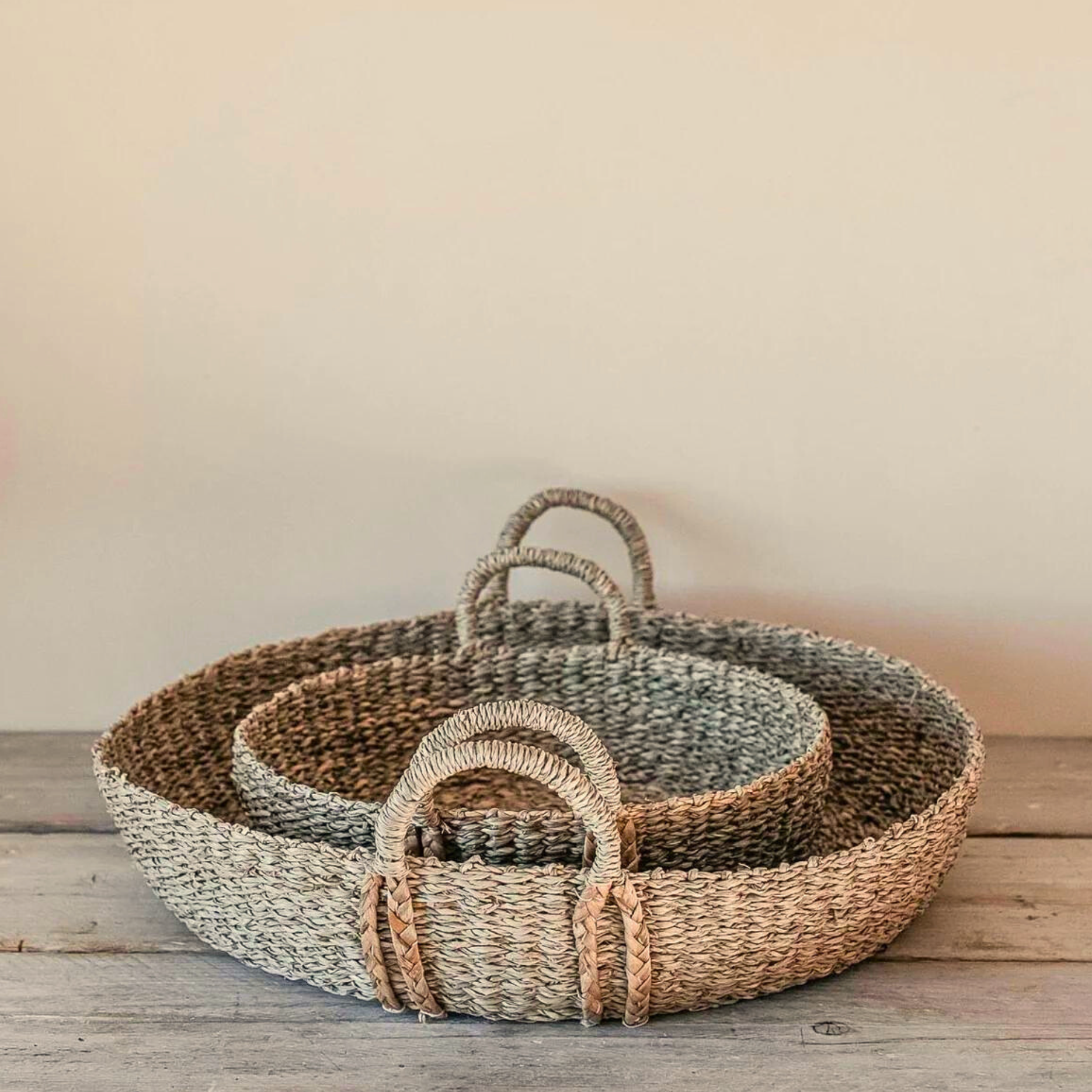 The Evelyn Seagrass Baskets stacked on a rustic wooden table. 