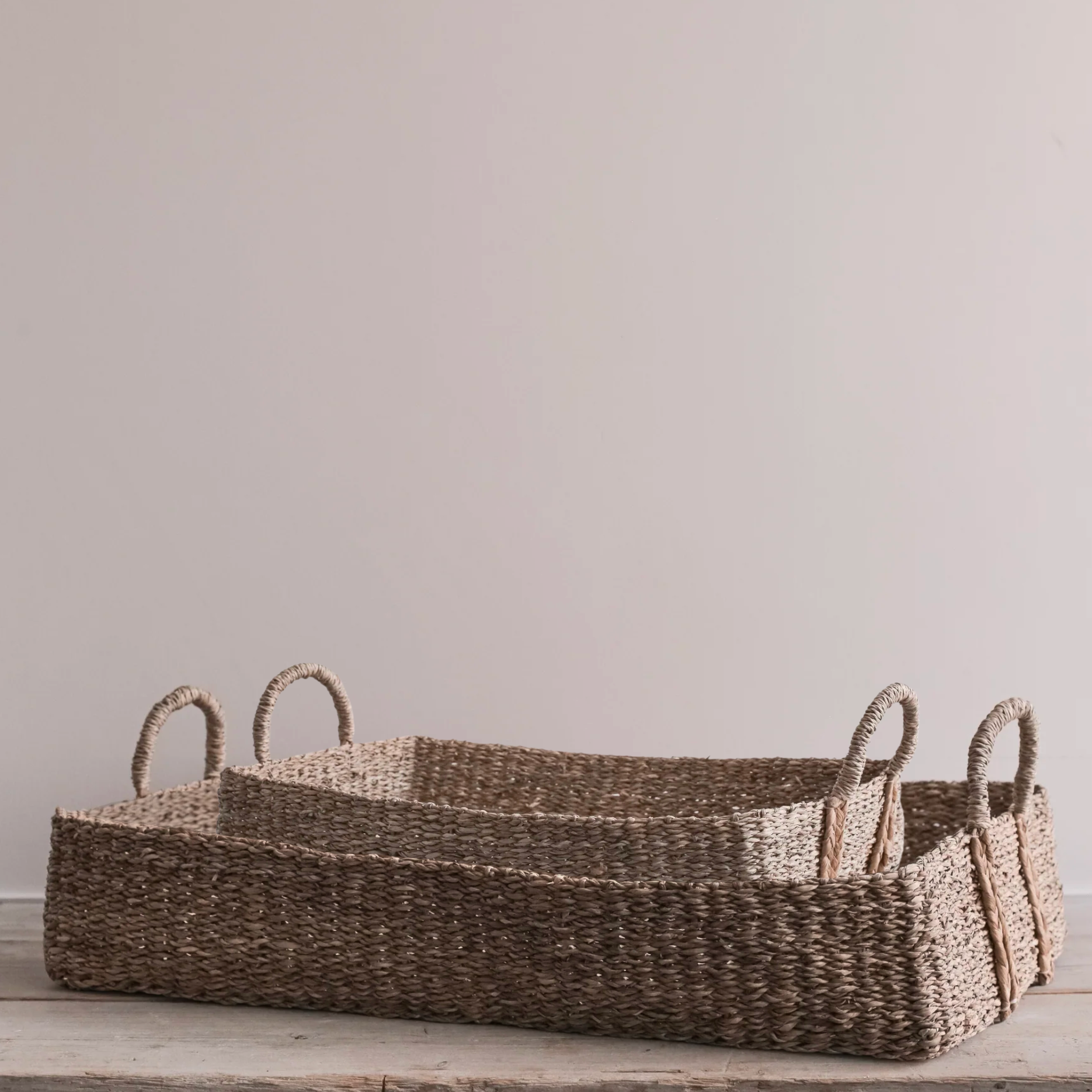 The Eliza Rectangular Seagrass Baskets - Set of Two stacked and on a rustic wooden table.