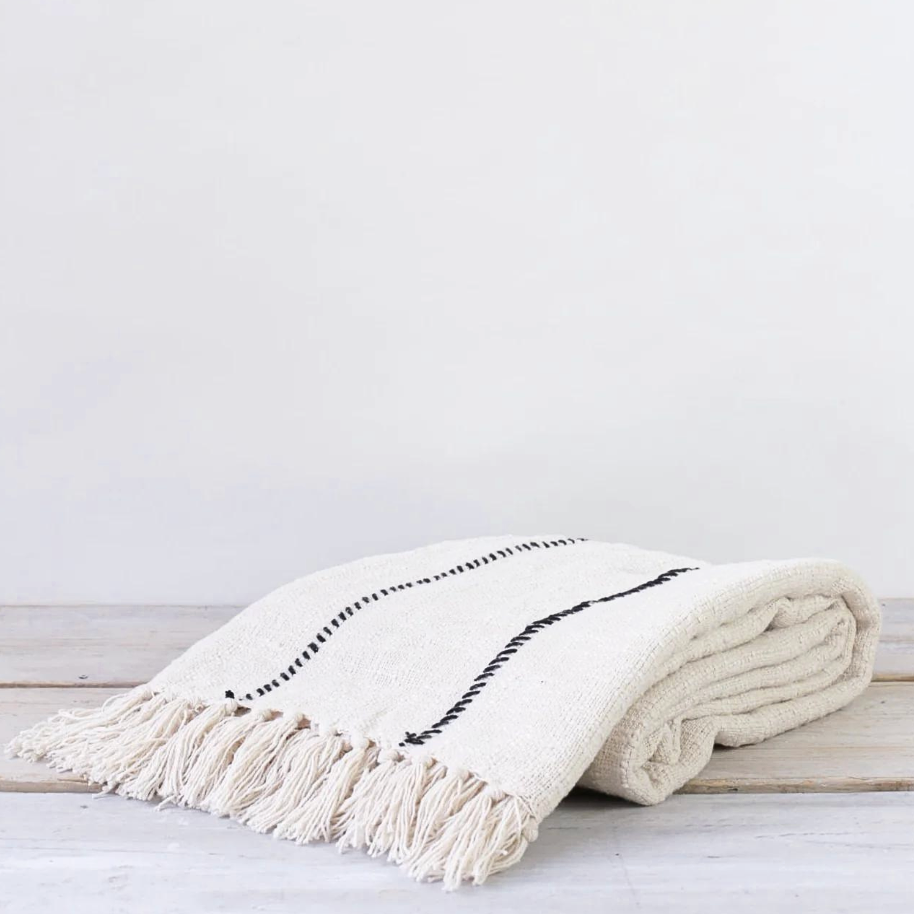 Folded neutral striped throw blanket with knotted tassels, folded on a rustic wooden table.