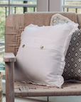 A white ruffle cushion with buttons paired with a green patterned cushion are paired on a woven armchair.