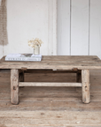 A Reclaimed Wood Coffee Table against a rustic white wooden wall.