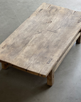 A rustic reclaimed coffee table on a cement floor.