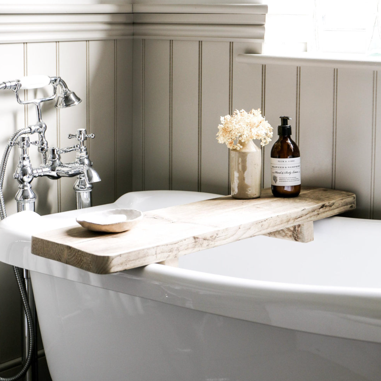 A chunky reclaimed bath board with a soap bottle and small vase with dried flowers in a bathroom.