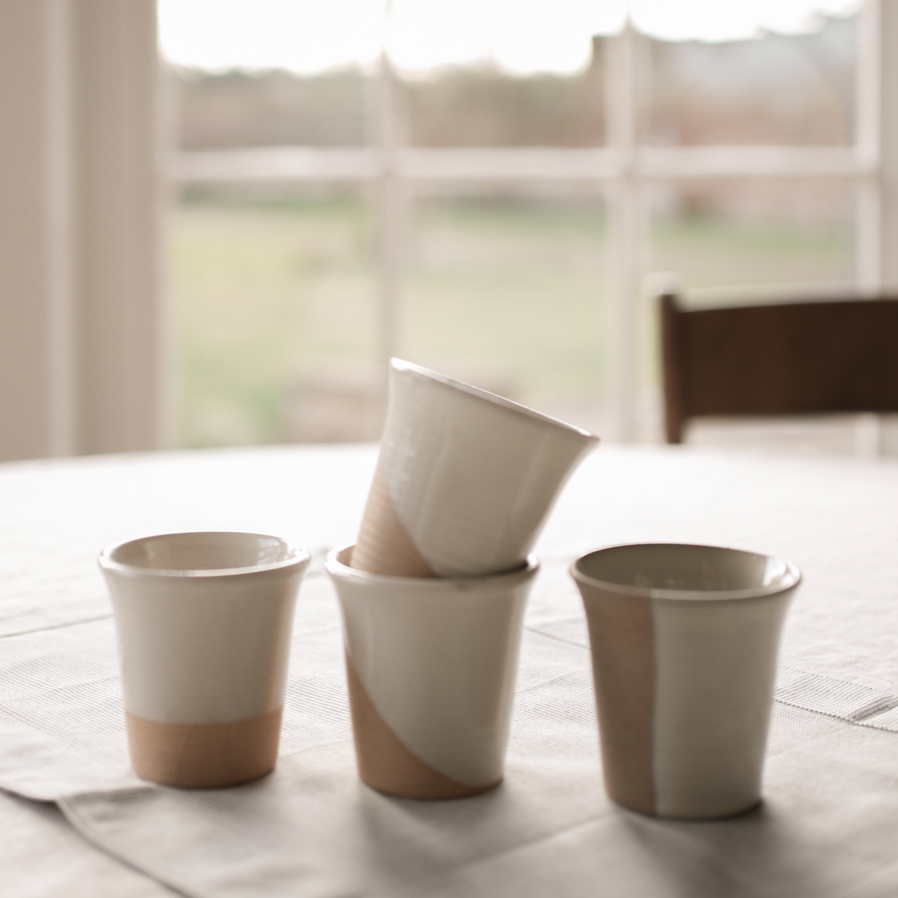 Stoneware Coffee Cups on a linen covered table in front of a window.