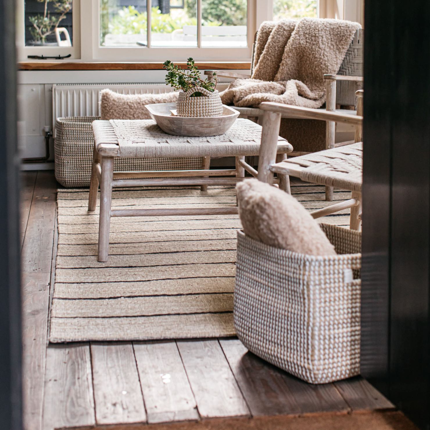 A striped jute rug with a wooden armchair and woven coffee table.