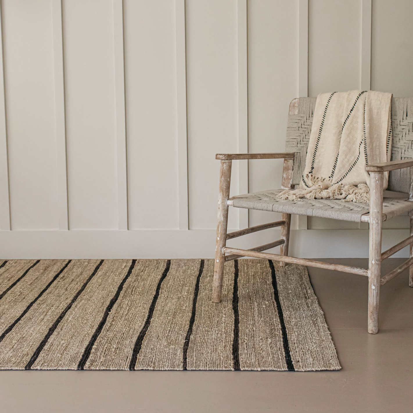A striped jute rug with a wooden armchair. 