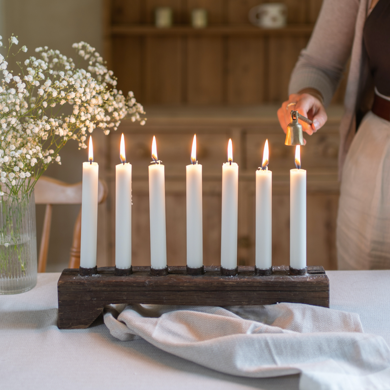 A wooden candle holder holding seven lit dinner candles.