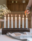 A wooden candle holder holding seven lit dinner candles.