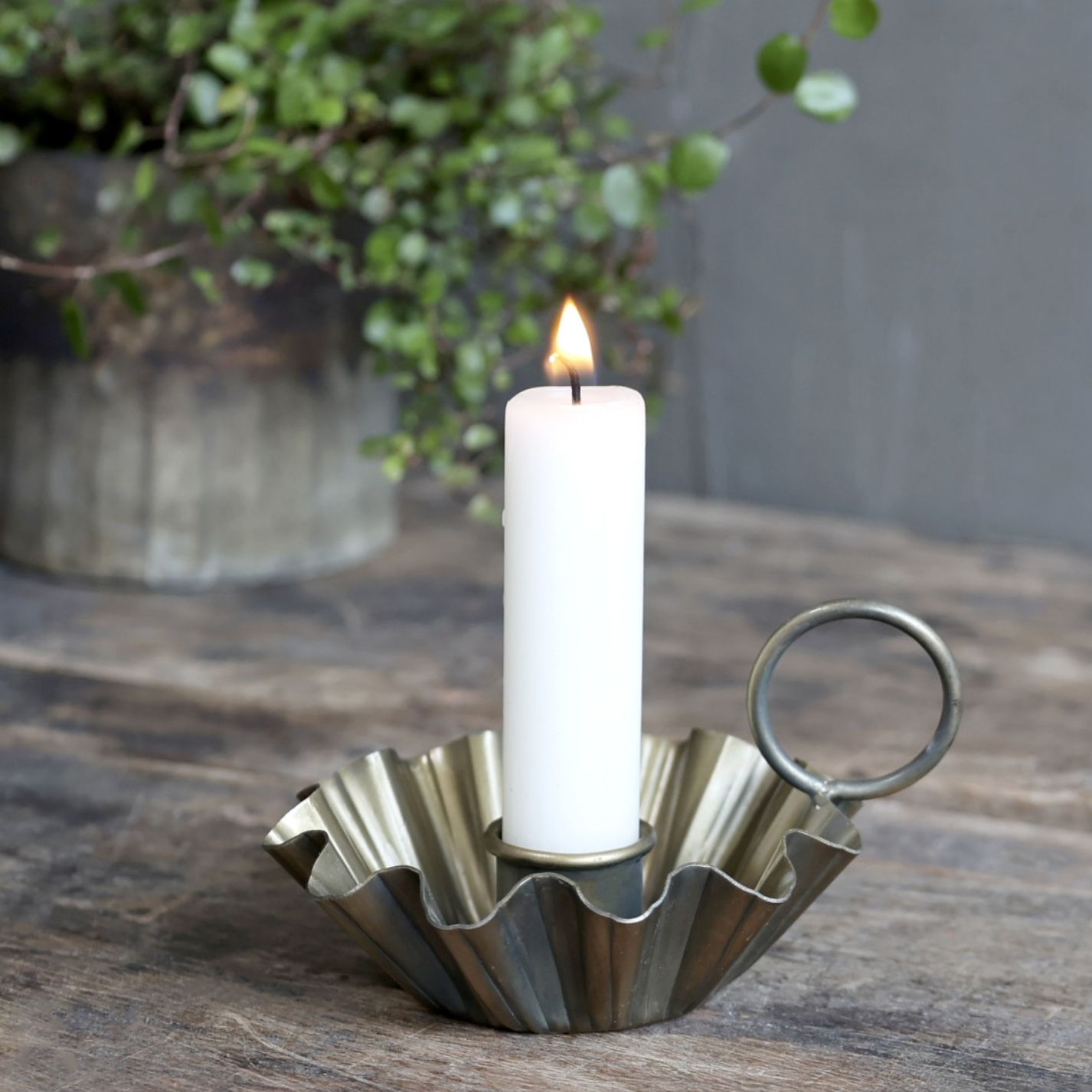 An antique brass candlestick holder with a white lit dinner candle.