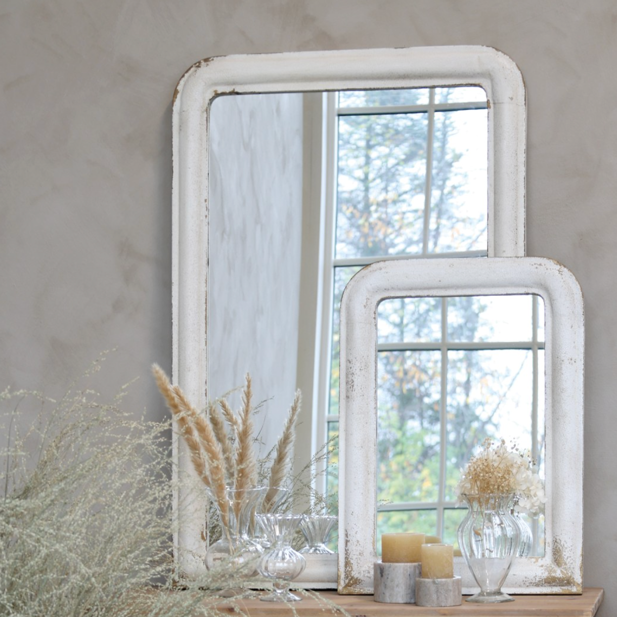Two distressed white mirrors leaning against a wall with dried flowers.