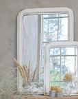 Two distressed white mirrors leaning against a wall with dried flowers.