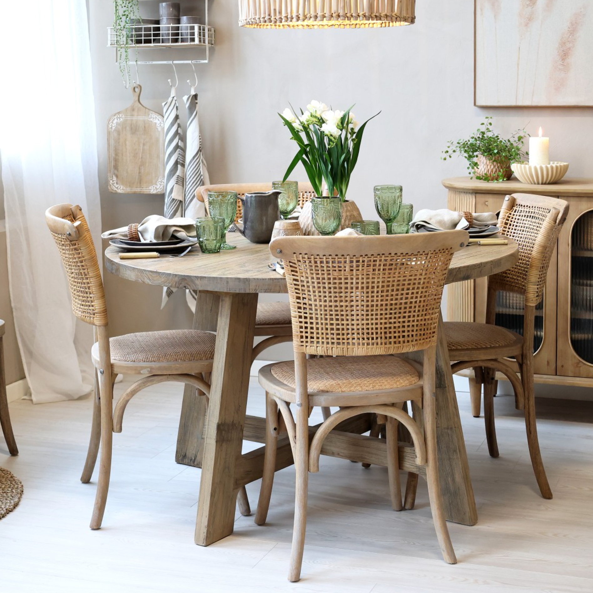 Round wood dining table with wicker backed chairs and crockery.