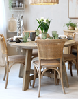 Round wood dining table with wicker backed chairs and crockery.