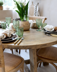 Round wood dining table with wicker backed chairs and crockery.