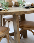 Round wood dining table with wicker backed chairs and crockery.