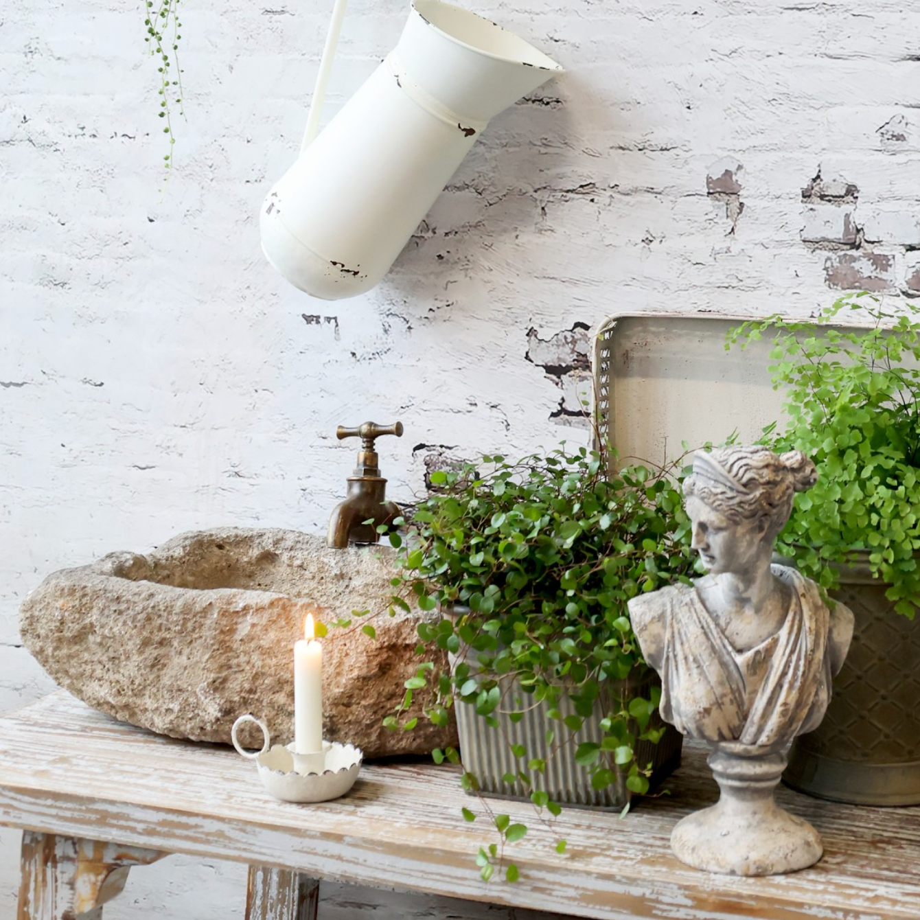 Candle Stick Holder with antique white finish and lit dinner candle. next to stone sink with plants.