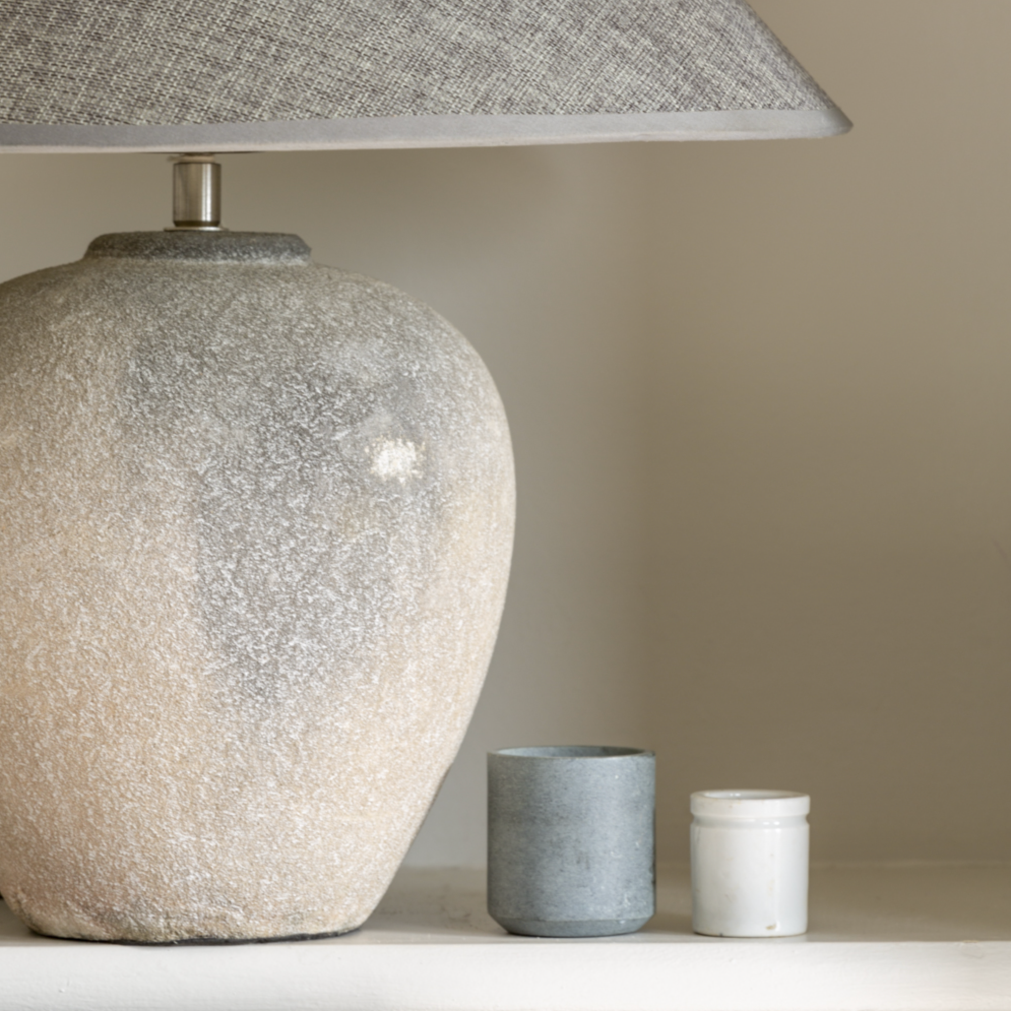 Stone coloured Ceramic Lamp with grey Shade on a shelf in a bedroom.