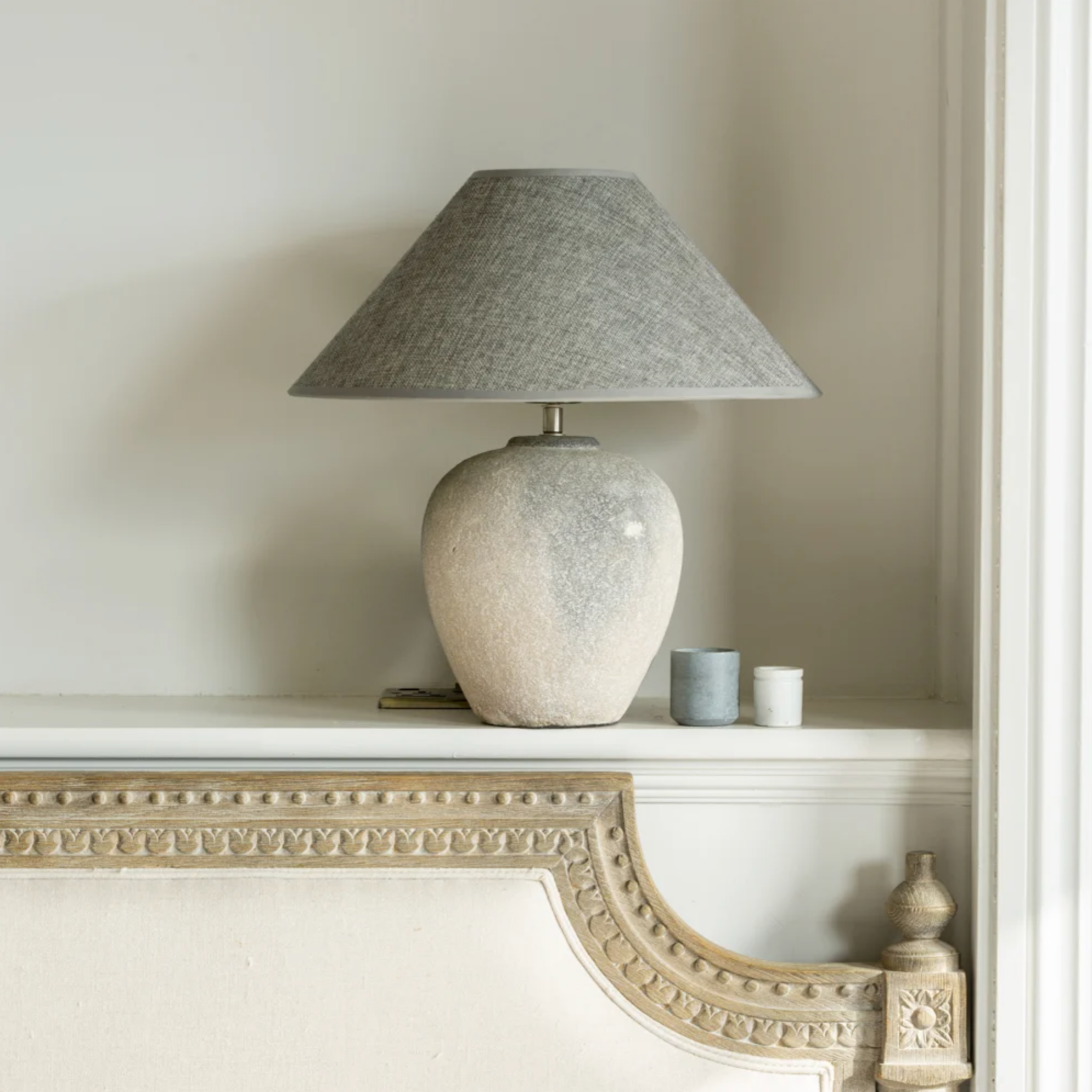 Stone coloured Ceramic Lamp with grey Shade on a shelf in a bedroom.