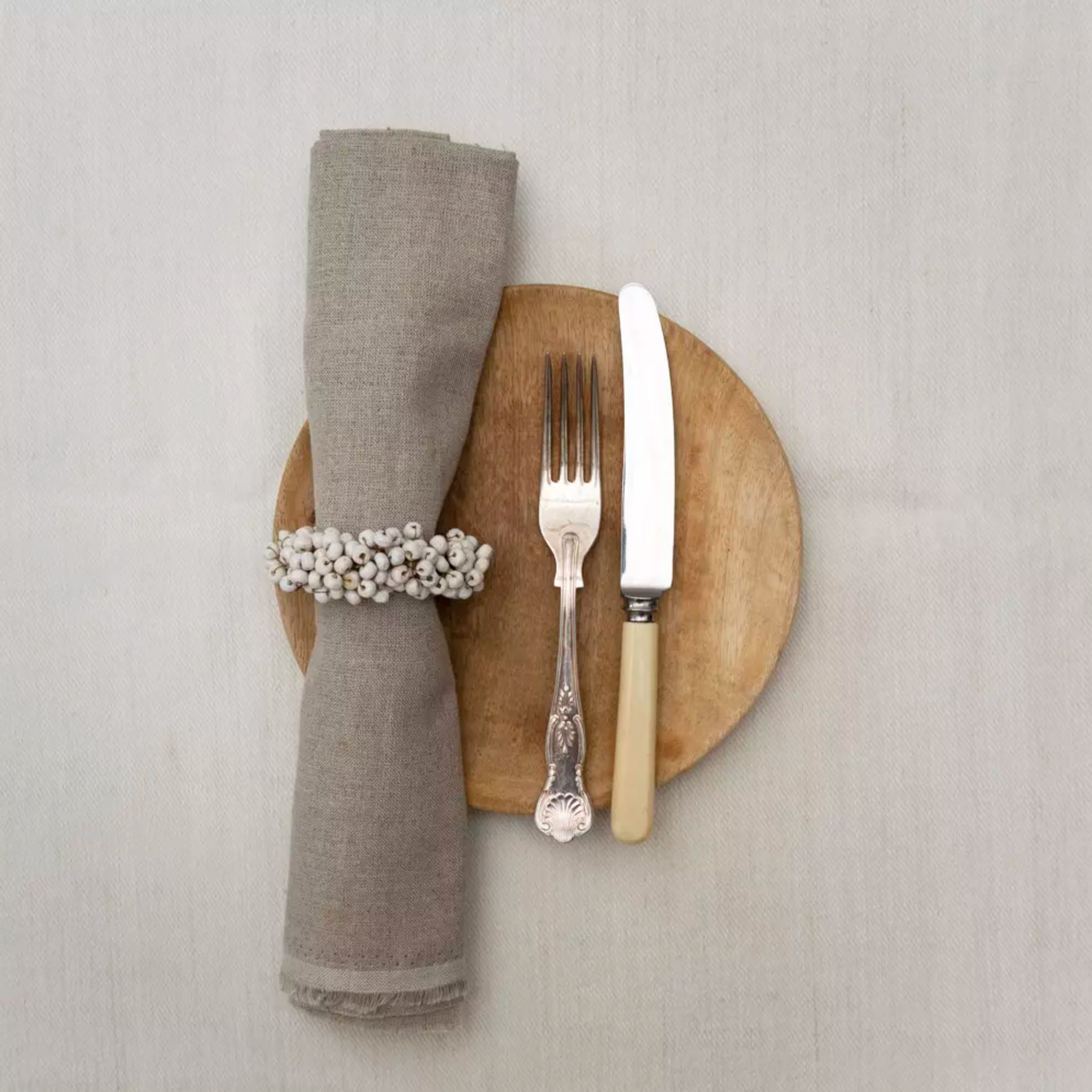 Wooden Napkin Ring with White Berries on a wooden plate with a knife and fork.