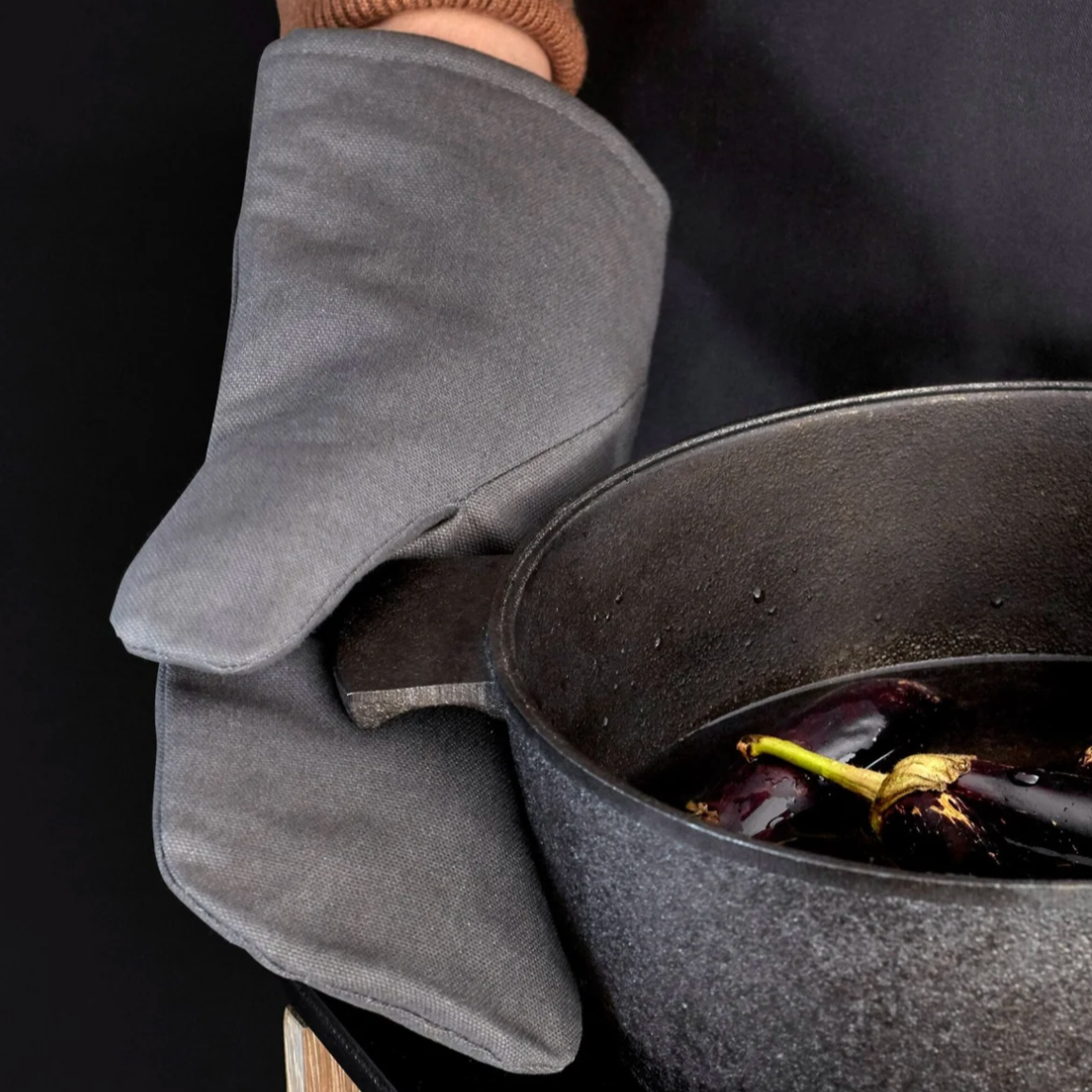 Dark grey oven glove on hand, holding a black skillet.