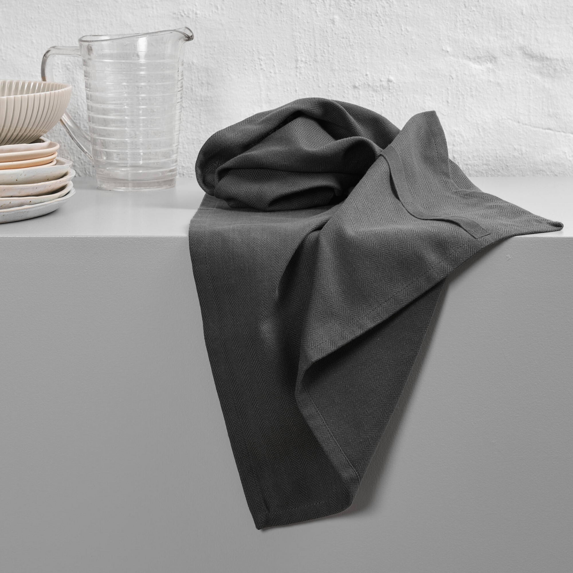 Dark grey towel scrunched on a surface with plates and a glass jug.