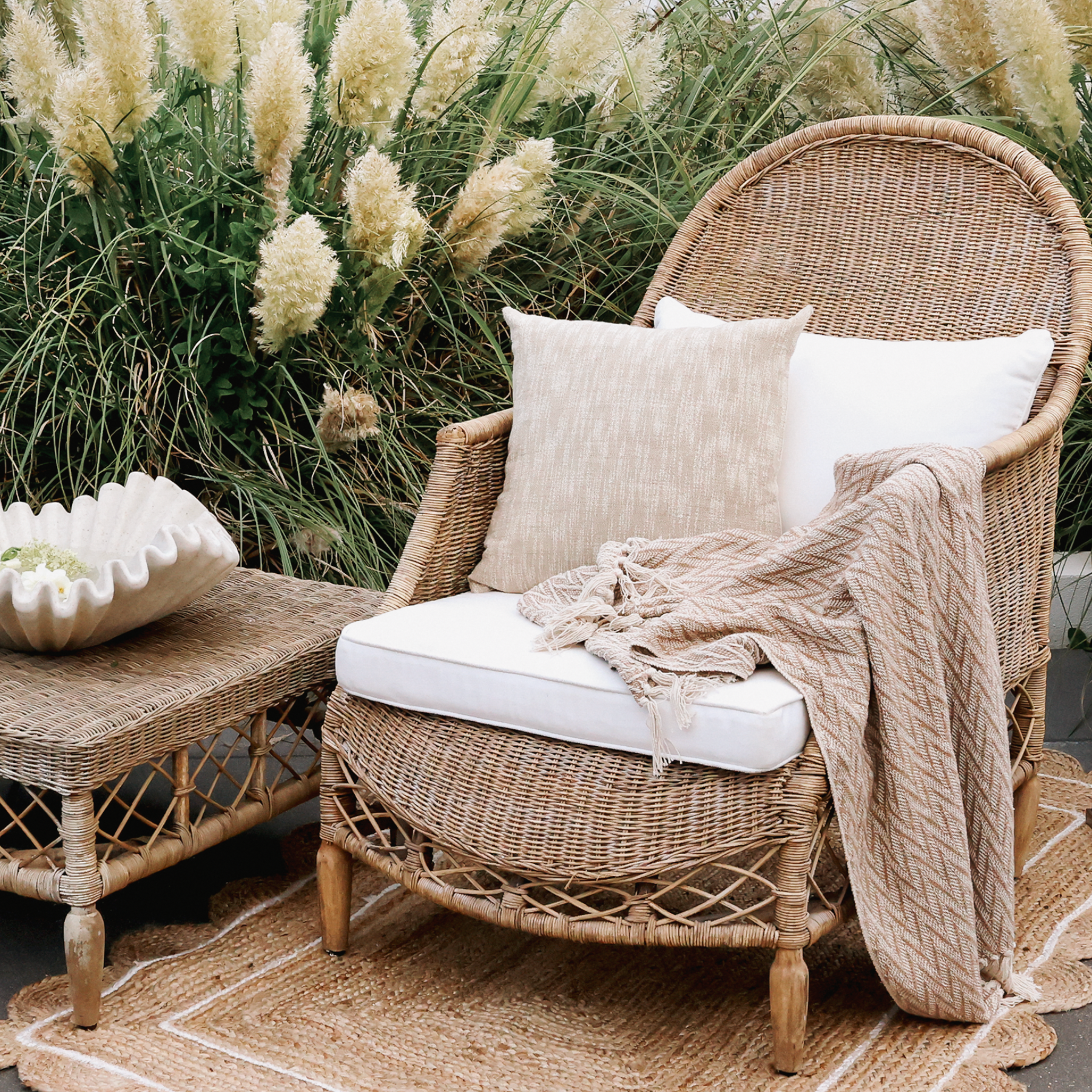 an outdoor living space with rattan armchair, jute rug and pampas grass.