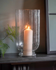 Glass hurricane vase filled with lit candle on a hearth. 