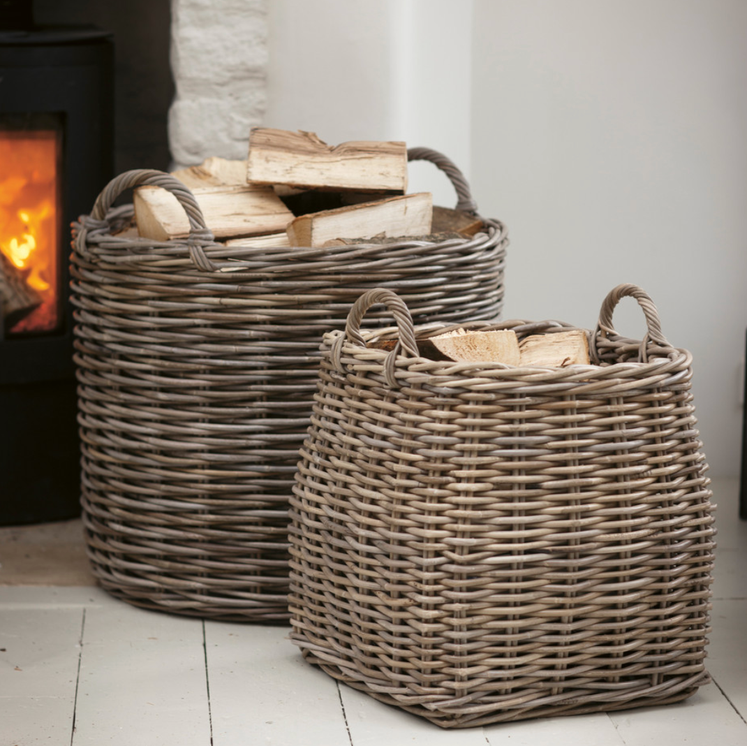 2 woven rattan log baskets, filled with logs in front of a fire.