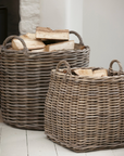 2 woven rattan log baskets, filled with logs in front of a fire.