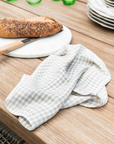 Natural gingham linen napkin folded up on table with bread board and knife.