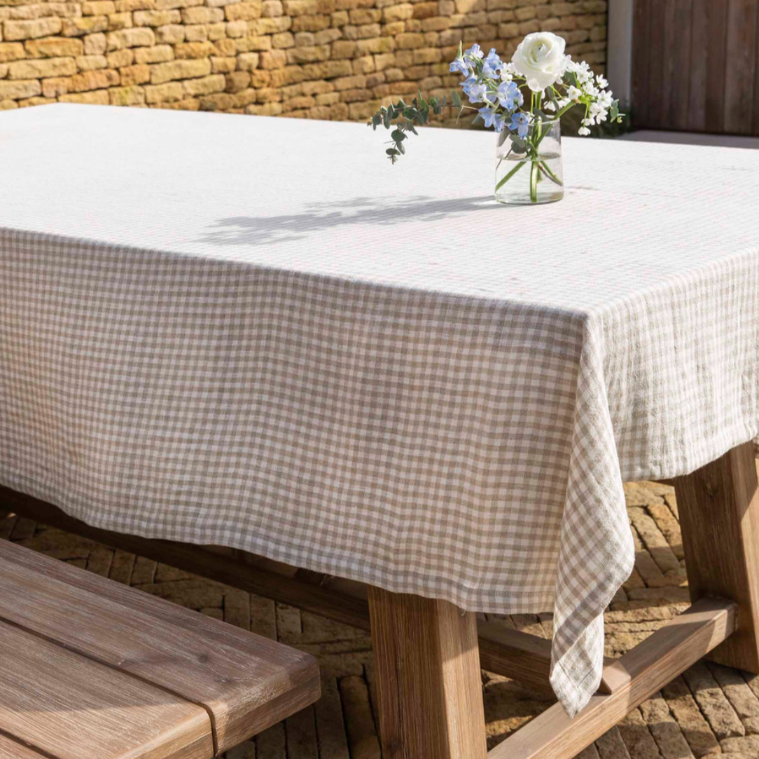 Natural gingham checked linen tablecloth on wooden table with vase and flower.