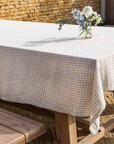 Natural gingham checked linen tablecloth on wooden table with vase and flower.