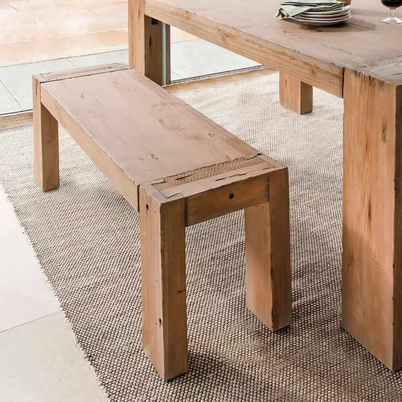 Close up of wooden dining bench, next to wooden dining table on a neutral rug.