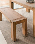 Close up of wooden dining bench, next to wooden dining table on a neutral rug.