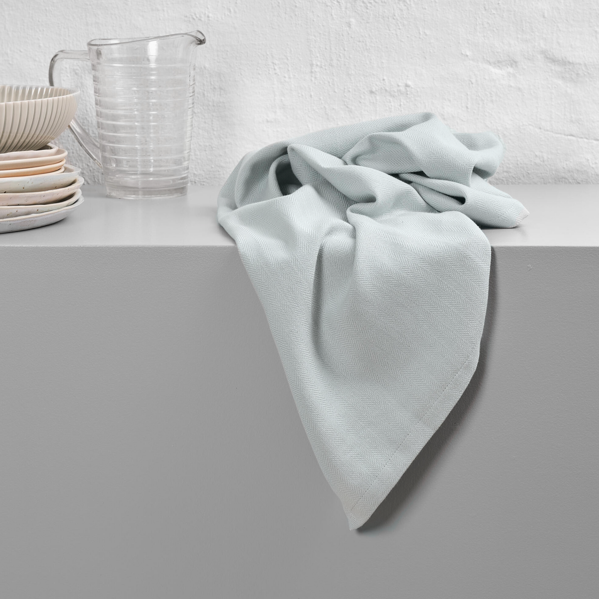 Sky blue kitchen towel scrunched up on surface with plates and glass jug.