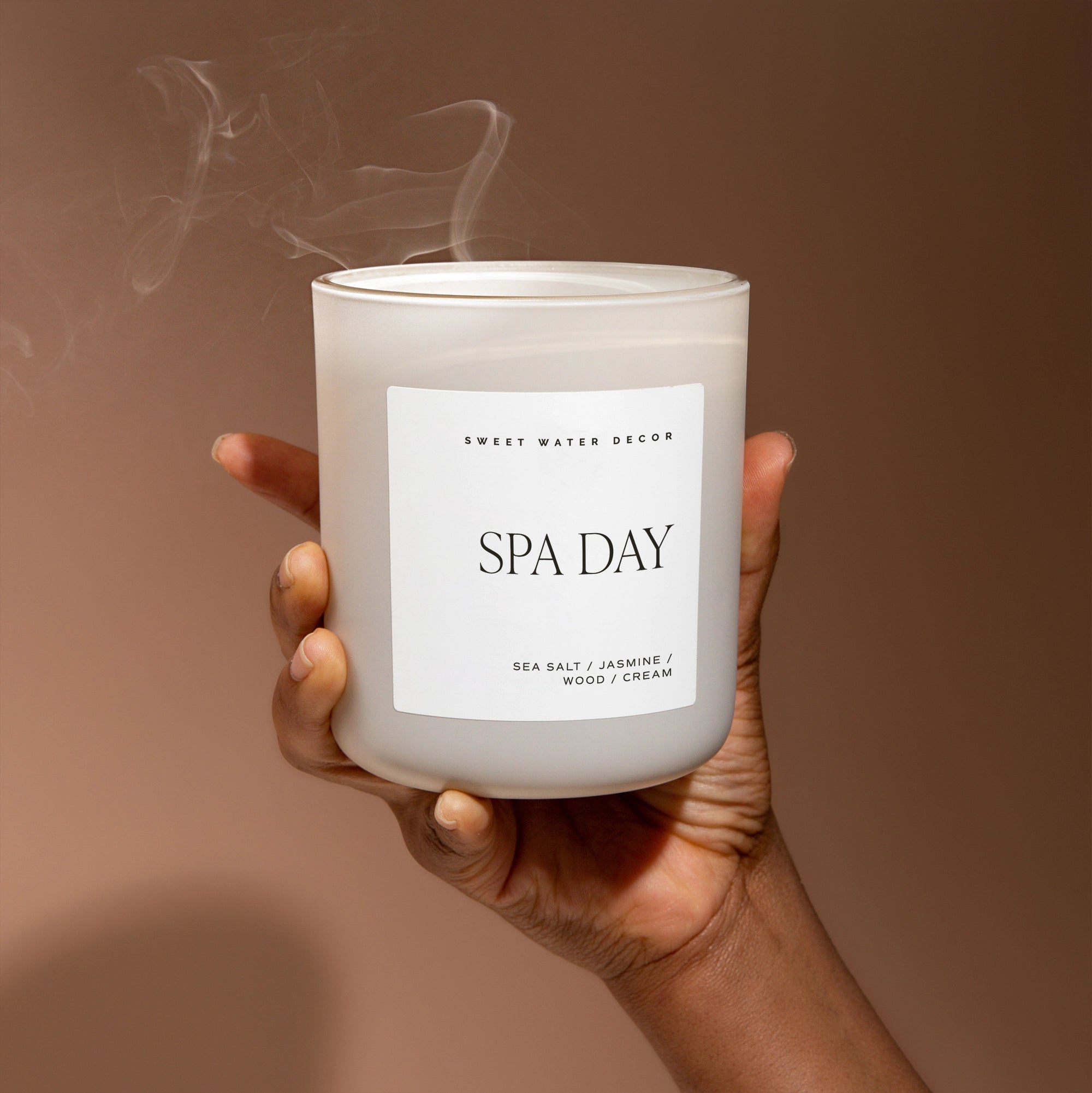 Large matt white soy candle, held up in one hand with blown out smoke coming off. 