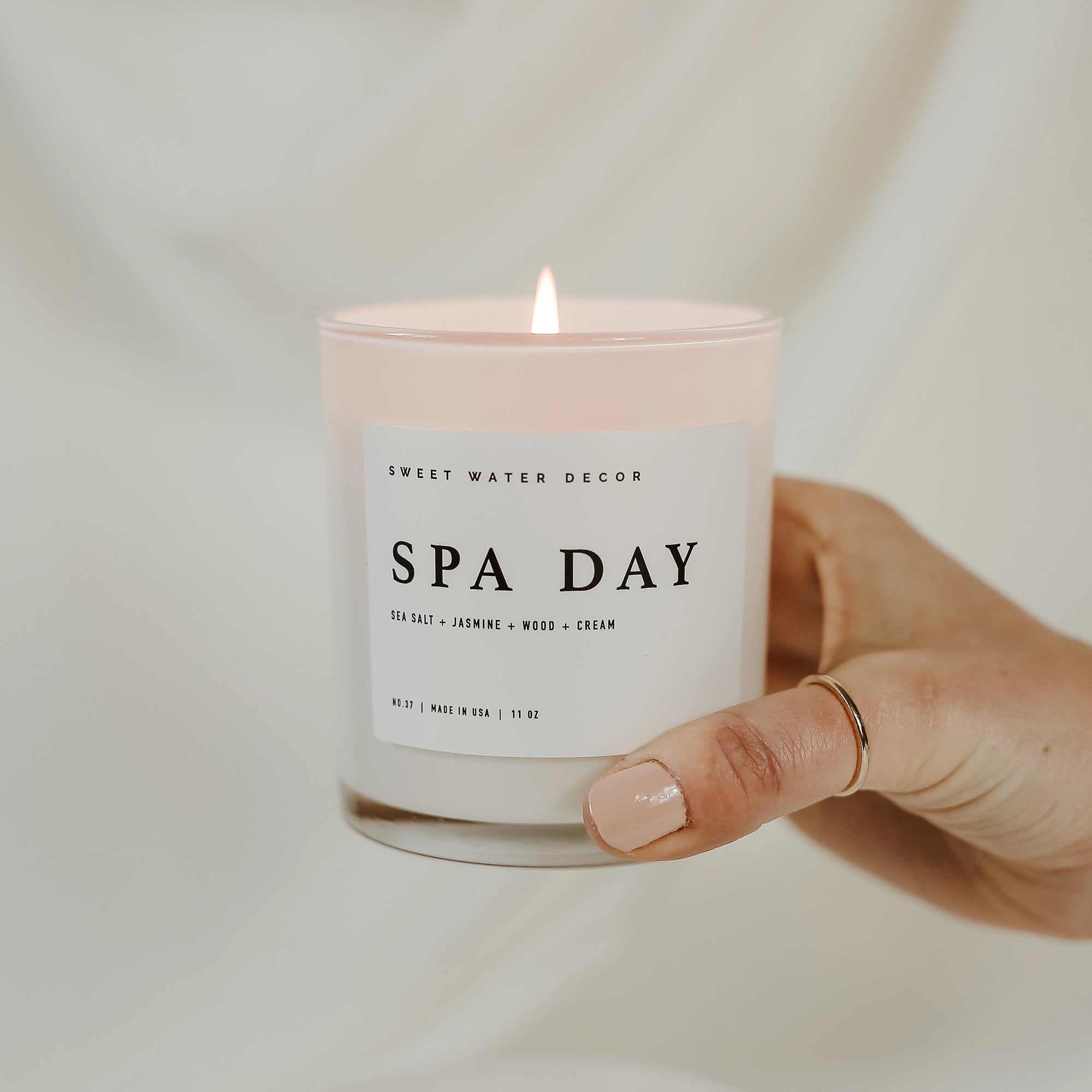 &#39;Spa Day&#39; soy candle lit and held up in one hand.