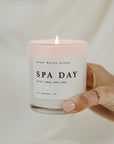 'Spa Day' soy candle lit and held up in one hand.