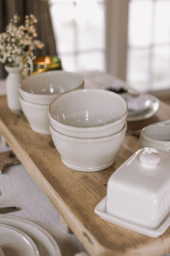 white cereal bowls on wooden serving plank with butter dish and flowers.